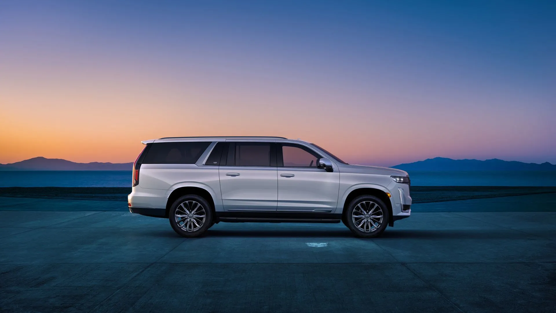 2024 Cadillac Escalade ESV màu trắng được chụp từ góc nhìn ngang tĩnh, đỗ xe vào lúc hoàng hôn với cảnh núi non phía sau.