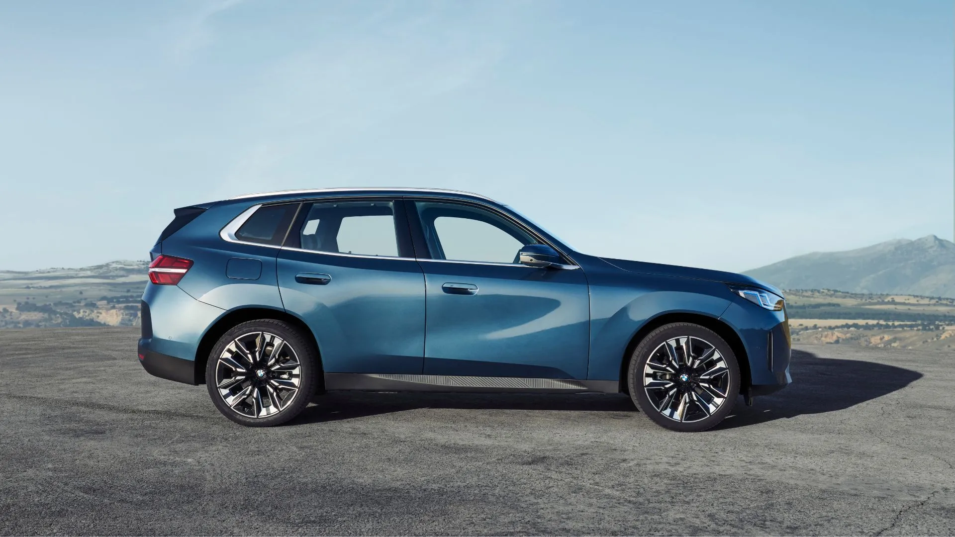 Ảnh chụp góc nghiêng thân xe BMW X3 2025 màu xanh đậu trên sỏi.