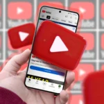 Bàn tay cầm điện thoại hiển thị logo YouTube, minh họa trải nghiệm người dùng với các tính năng mới trên nền tảng.