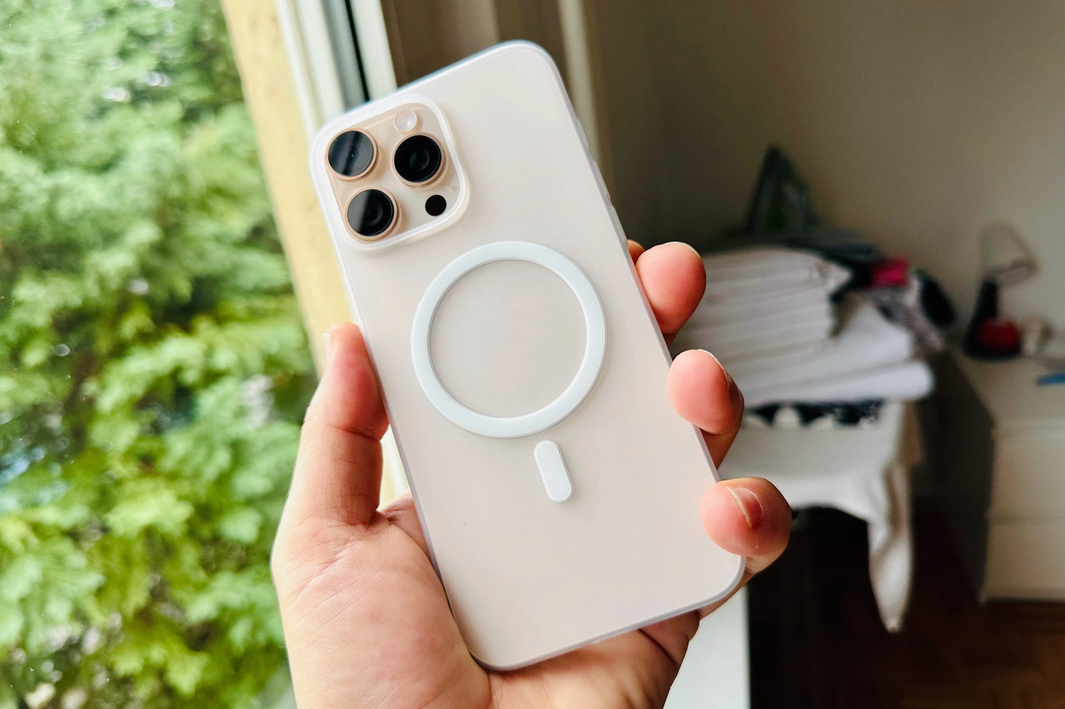 Bàn tay đang cầm iPhone 16 Pro Max màu Titan sa mạc với ốp lưng trong suốt Totallee MagSafe, khoe mặt lưng ba camera