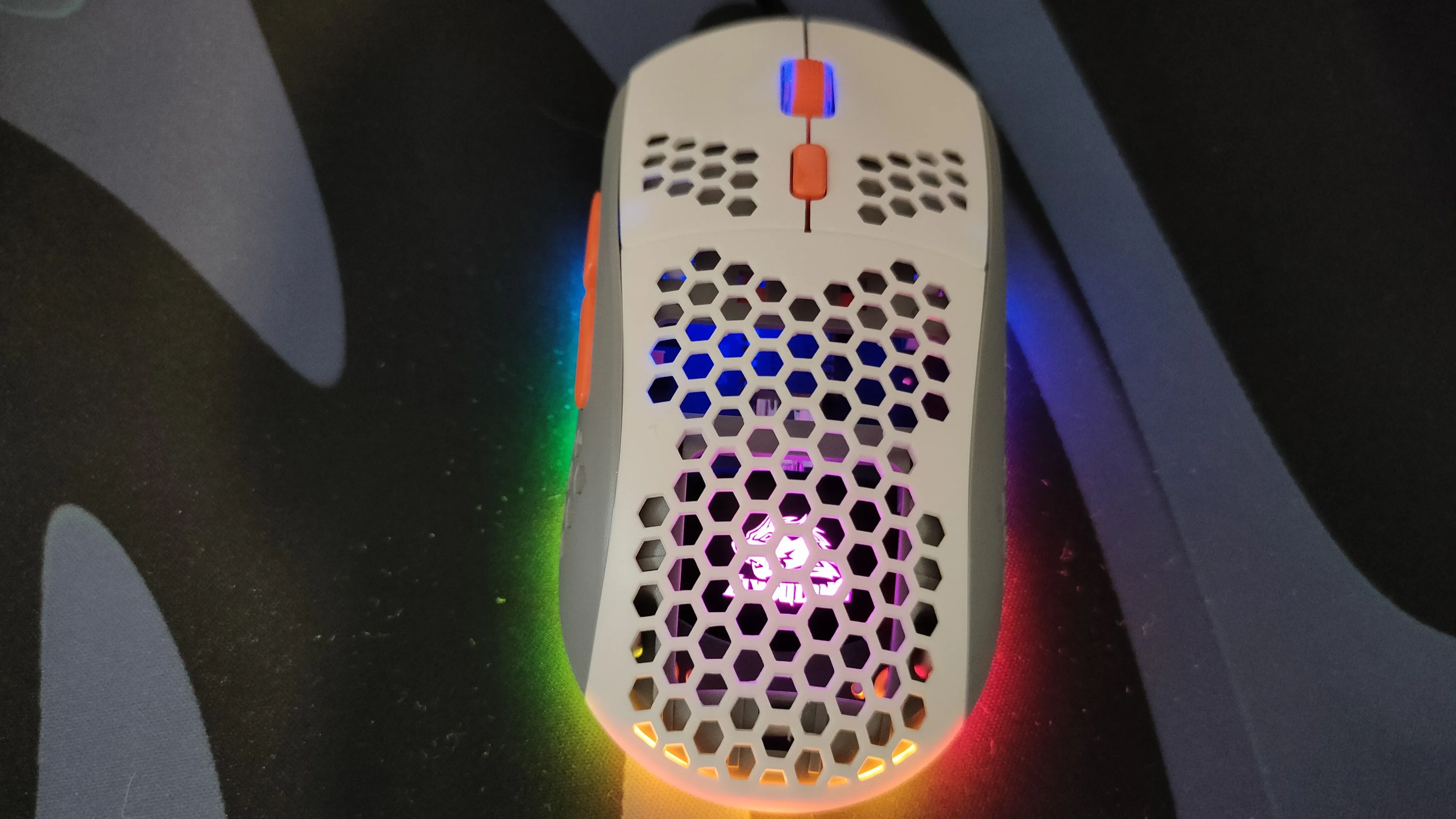 Chuột gaming màu trắng với thiết kế vỏ tổ ong và đèn RGB, minh họa cho loại chuột có lỗ.