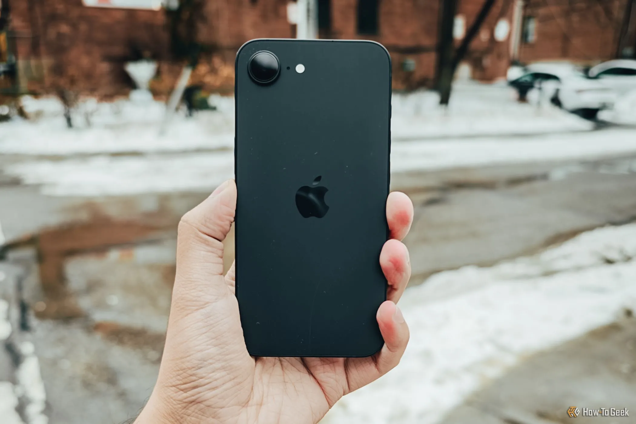 Điện thoại iPhone 16e màu trắng được cầm trên tay ngoài đường, thể hiện thiết kế tối giản và gọn nhẹ