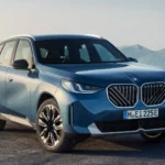 Hình ảnh cận cảnh phía trước của xe BMW X3 2025 màu xanh đậu trên nền sỏi.