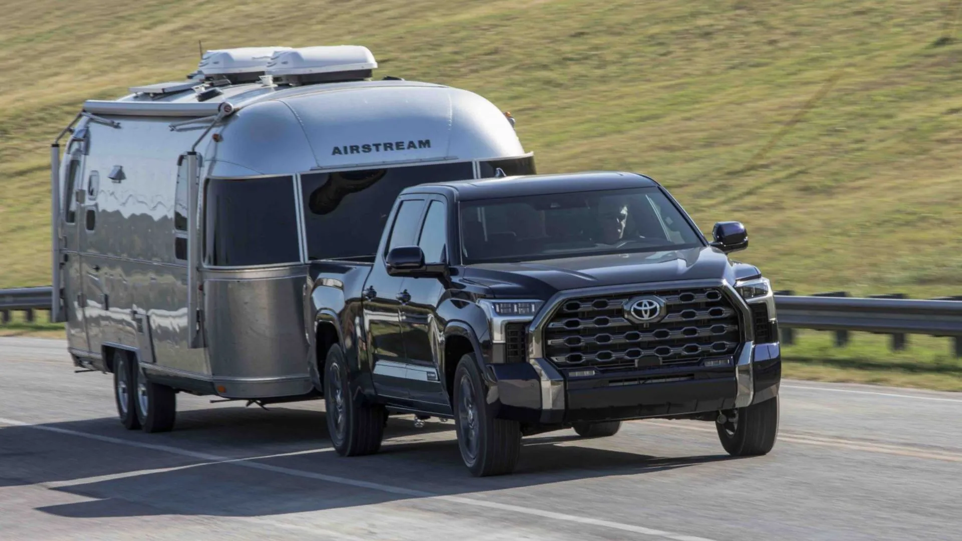 Hình ảnh chiếc Toyota Tundra Platinum Blueprint 2025 màu xanh đậm đang kéo rơ moóc trên con đường nông thôn.