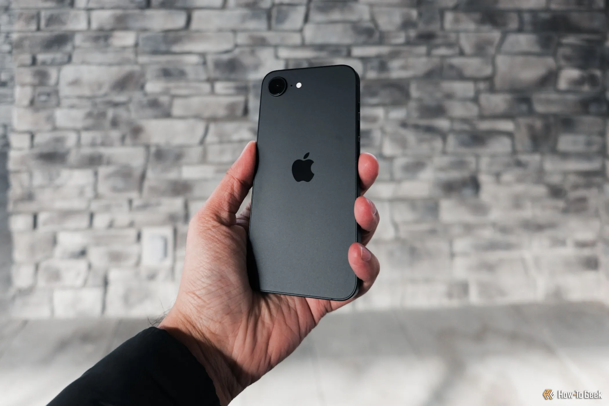 Hình ảnh mặt lưng và cạnh viền của iPhone 16e màu trắng trong tay, nhìn nghiêng