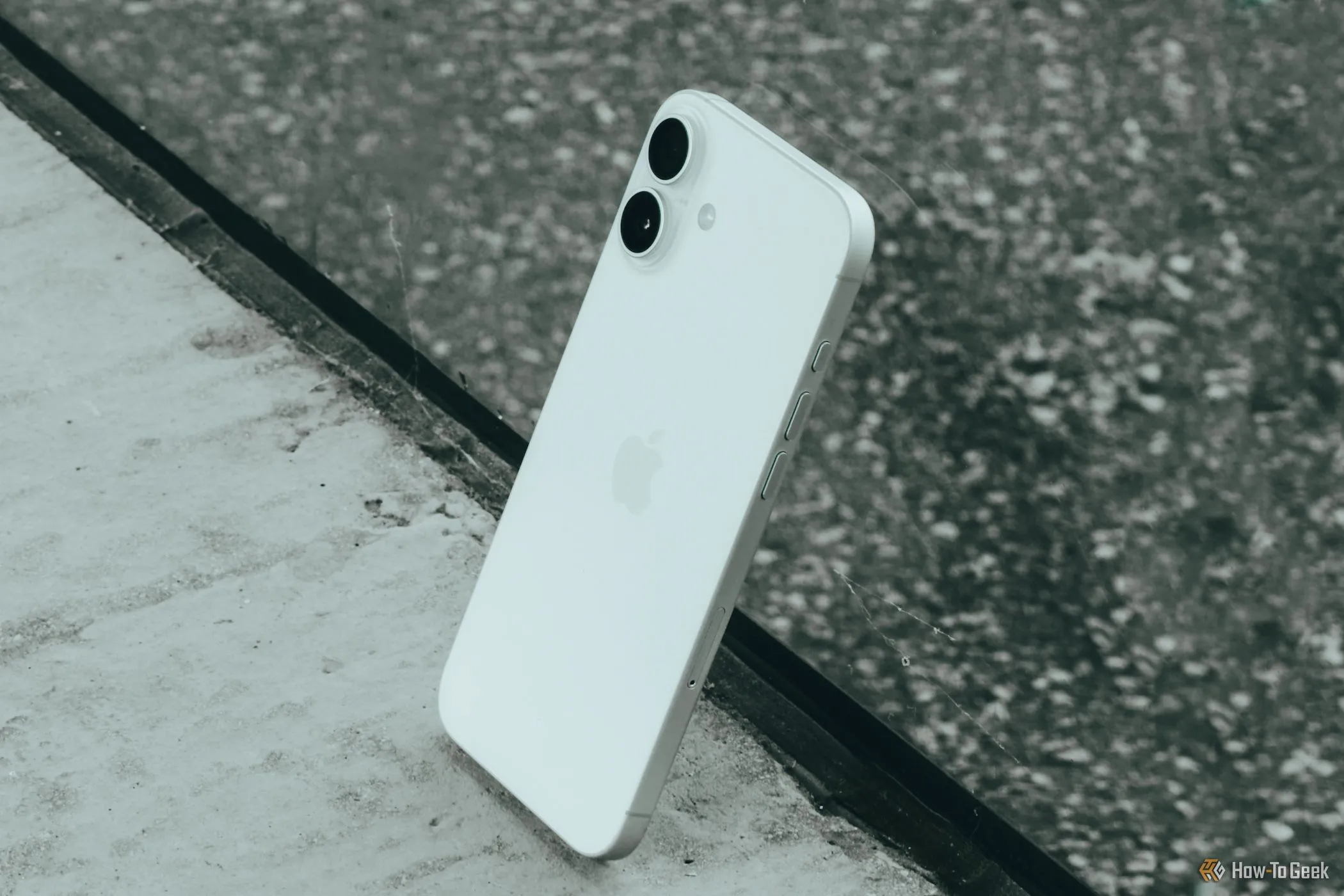 iPhone 16 Plus màu hồng được đặt nghiêng dựa vào tấm kính, thể hiện thiết kế và màu sắc
