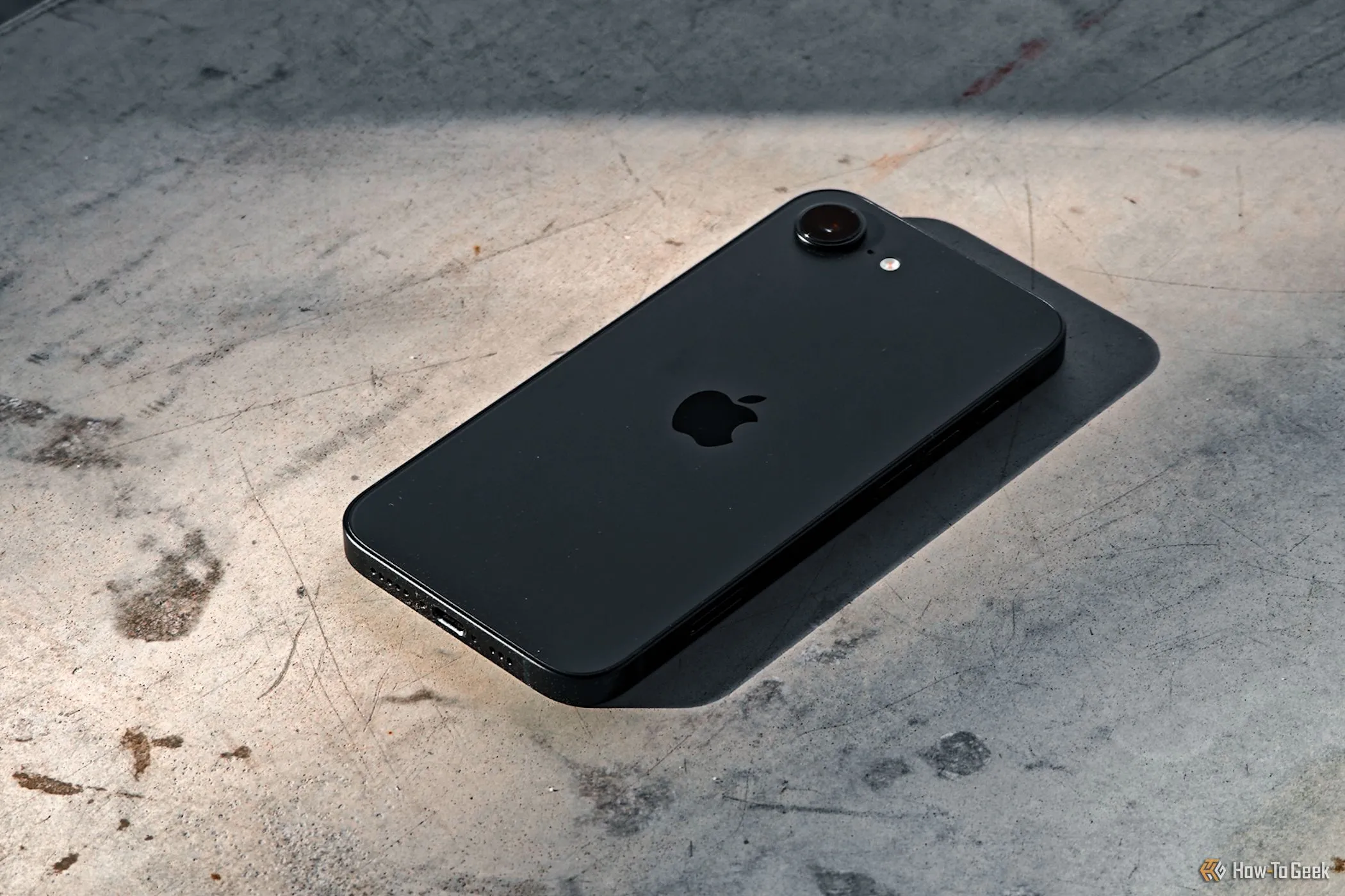 iPhone 16e màu trắng đặt úp mặt xuống trên nền bê tông, thể hiện độ bền và kiểu dáng phẳng