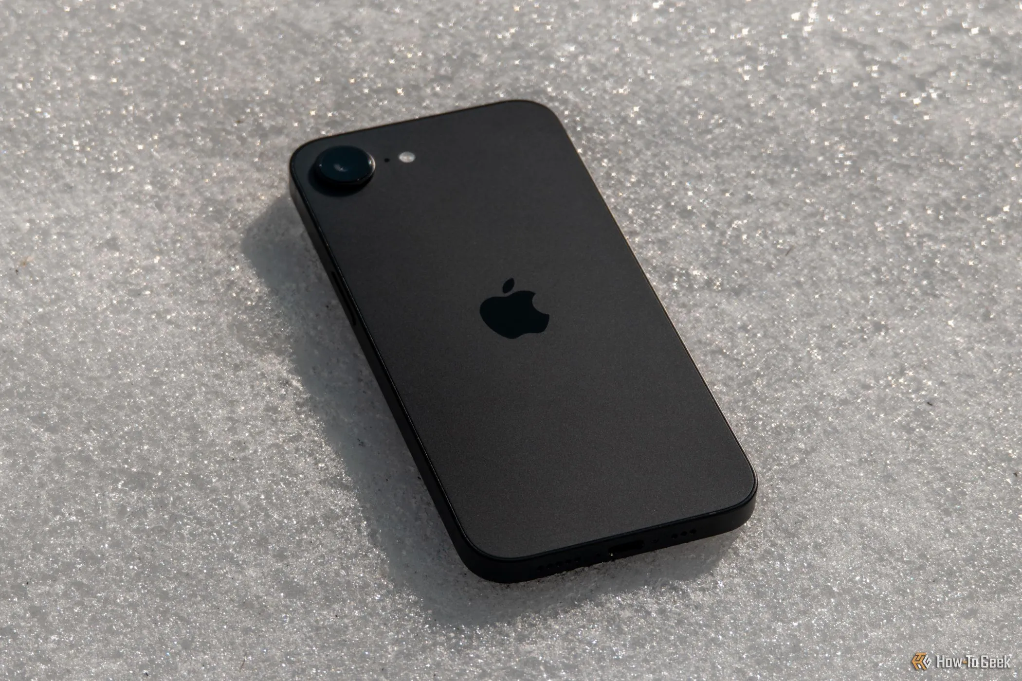 iPhone 16e màu trắng đặt úp mặt xuống trên nền tuyết, nổi bật thiết kế tối giản và mặt lưng nhám