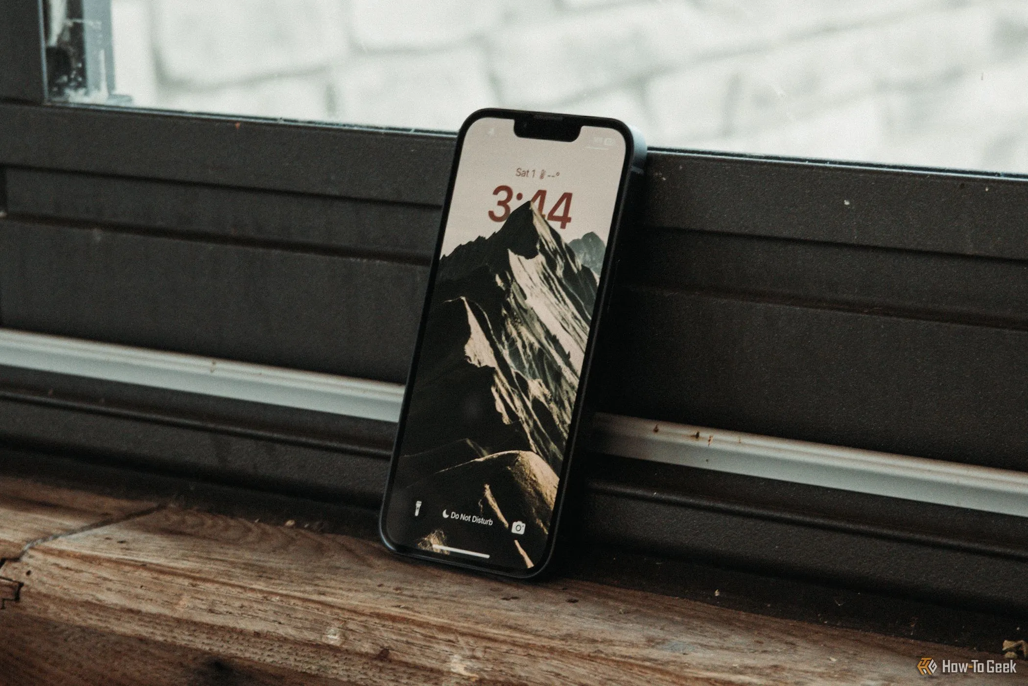 Màn hình khóa của iPhone 16e hiển thị ngày giờ, tựa vào cửa sổ