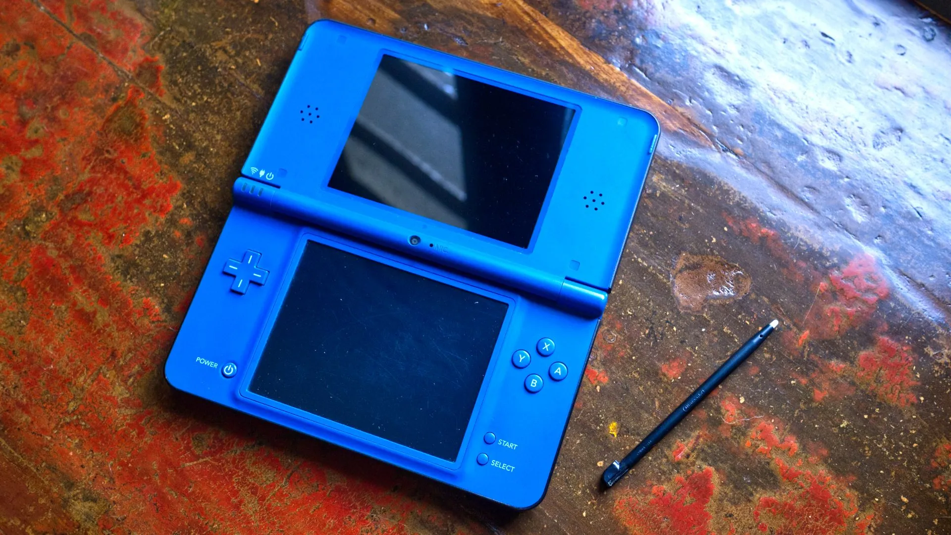 Máy chơi game cầm tay Nintendo DSi XL màu xanh mở ra với bút cảm ứng, minh họa cho công nghệ màn hình cảm ứng tiên phong của Nintendo DS.