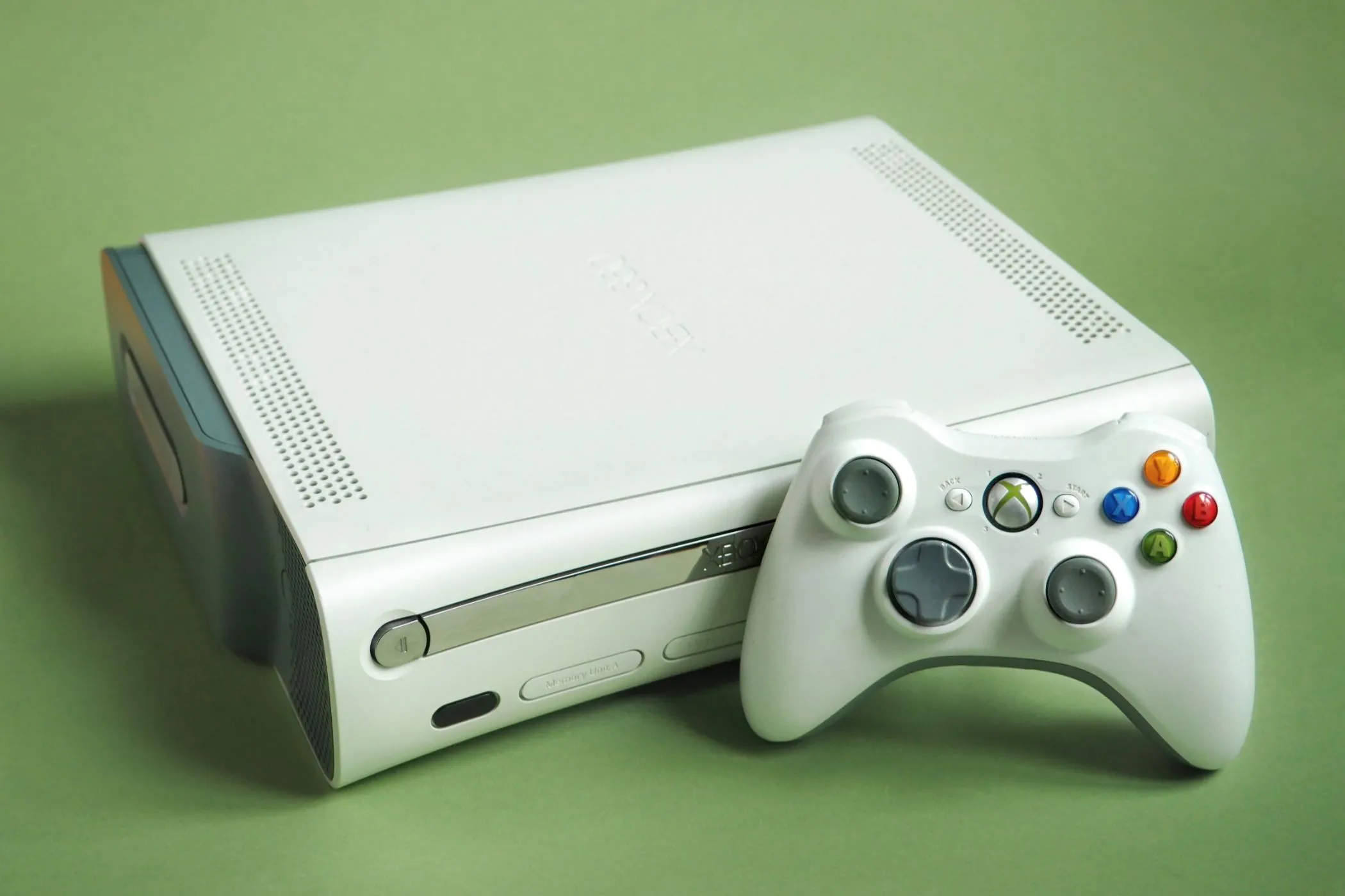 Một chiếc Xbox 360 màu trắng cùng với tay cầm điều khiển, đặt trên nền tối