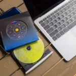 Một ổ đĩa CD/DVD gắn ngoài và đĩa nhạc CD đặt cạnh MacBook Air, biểu thị phương pháp chuyển nhạc từ đĩa vật lý.