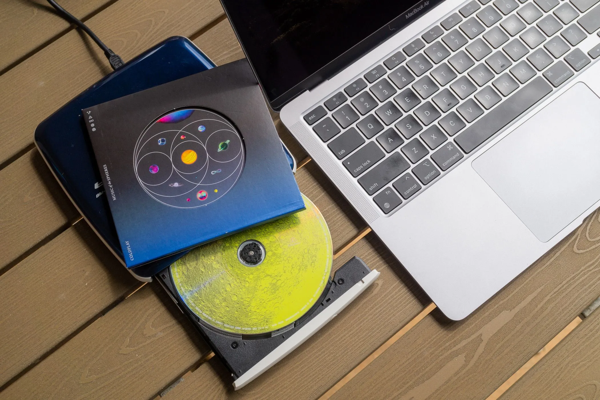 Một ổ đĩa CD/DVD gắn ngoài và đĩa nhạc CD đặt cạnh MacBook Air, biểu thị phương pháp chuyển nhạc từ đĩa vật lý.