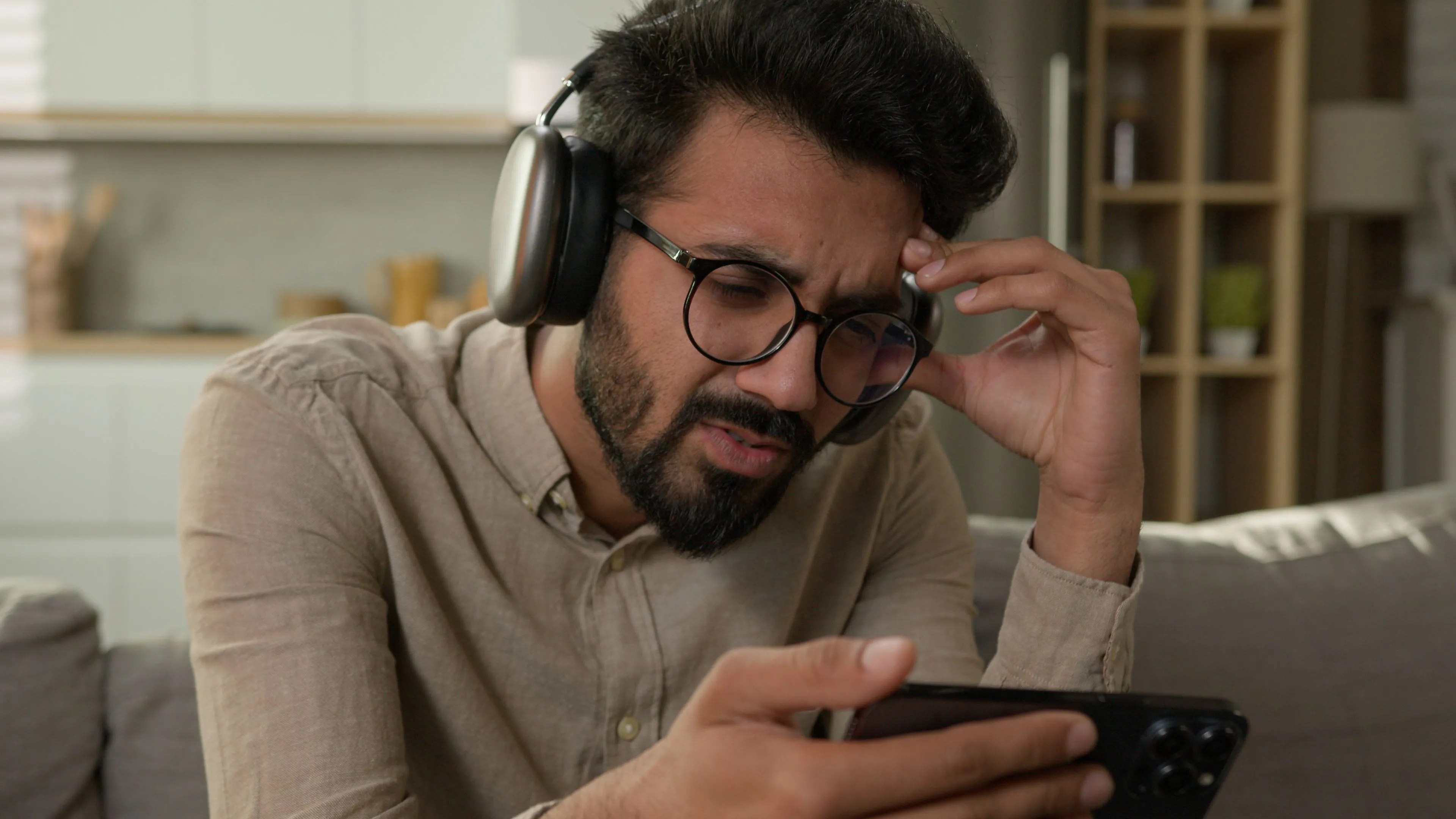 Người đàn ông trẻ tuổi đeo tai nghe AirPods Max, vẻ mặt thất vọng khi nhìn vào màn hình iPhone ở chế độ đen trắng, thể hiện sự xao nhãng do điện thoại