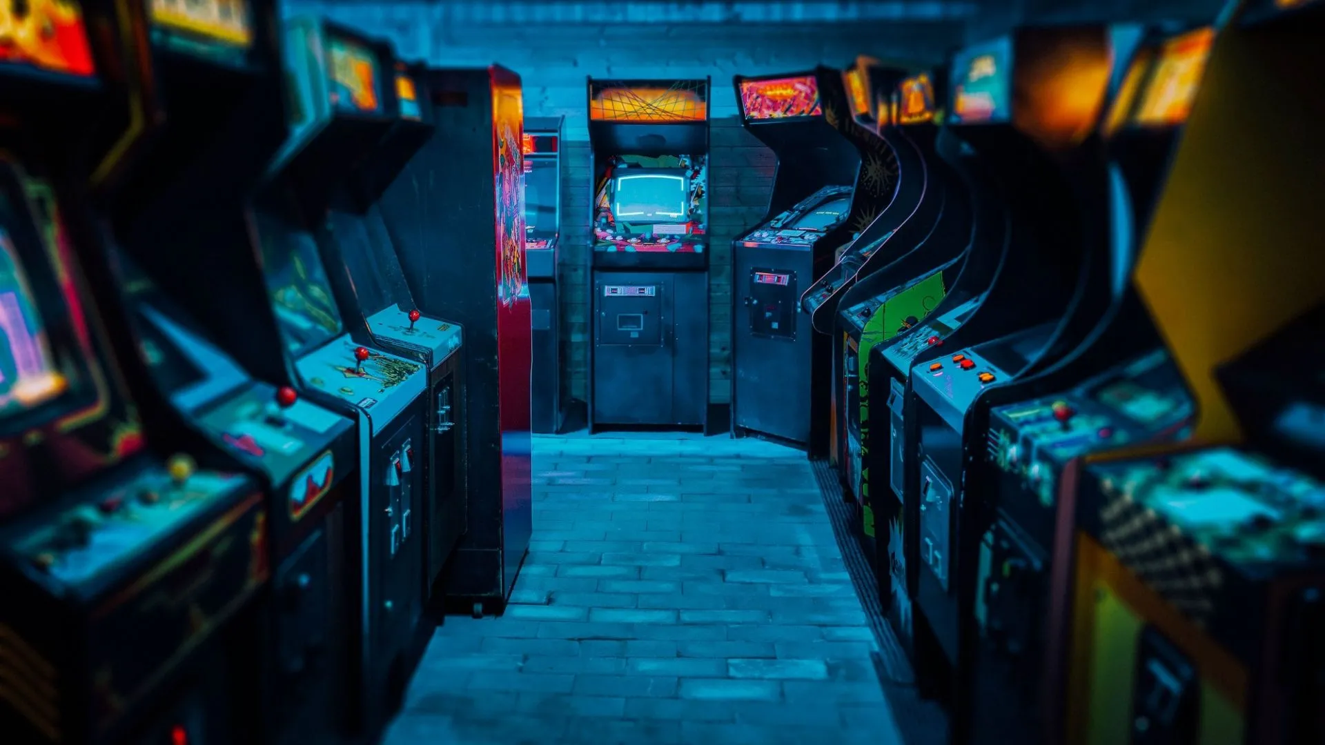 Những máy chơi game thùng arcade cổ điển trong căn phòng ánh sáng xanh, minh họa sự đa dạng của tay cầm game ngày xưa.