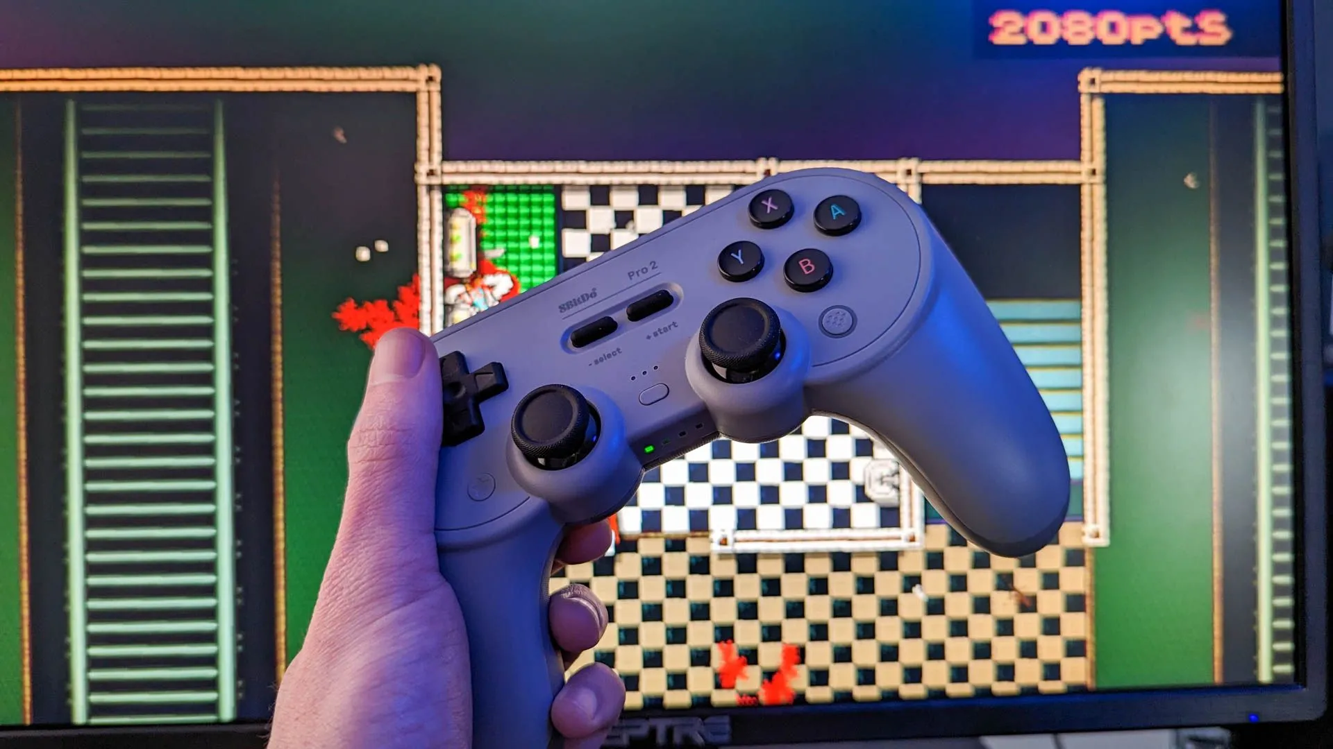 Tay cầm chơi game không dây 8Bitdo Pro 2 đặt cạnh màn hình máy tính, minh họa việc chơi game trên Linux.